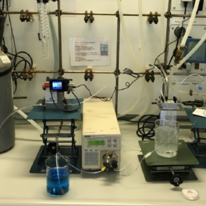 Coverbild zum Projekt "PhotoCarbFlow - Kontinuierliche Herstellung von neuen Hochleistungschemikalien aus nachwachsenden Rohstoffen und Kohlendioxid mit Sonnenlicht" (Laborbild mit einer Gasflasche, Zylinderkolben und Halterungen)