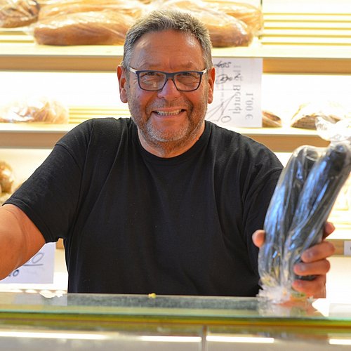 Das Bild zeigt einen Mann hinter der Verkaufstheke einer Bäckerei.